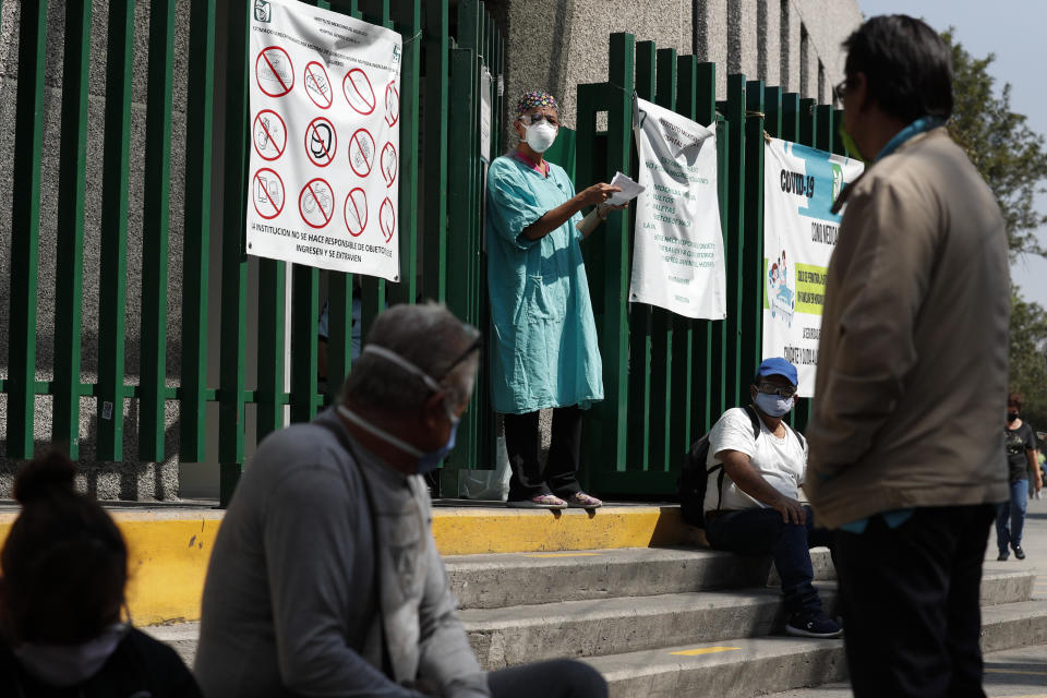 A hospital worker calls out a name from the gate, as relatives of hospitalized patients wait outside in hopes of receiving news of their loved ones, at a public hospital in the Iztapalapa district of Mexico City, Tuesday, May 5, 2020. Iztapalapa has the most confirmed cases of the new coronavirus within Mexico's densely populated capital, itself one of the hardest hit areas of the country with thousands of confirmed cases and around 500 deaths.(AP Photo/Rebecca Blackwell)