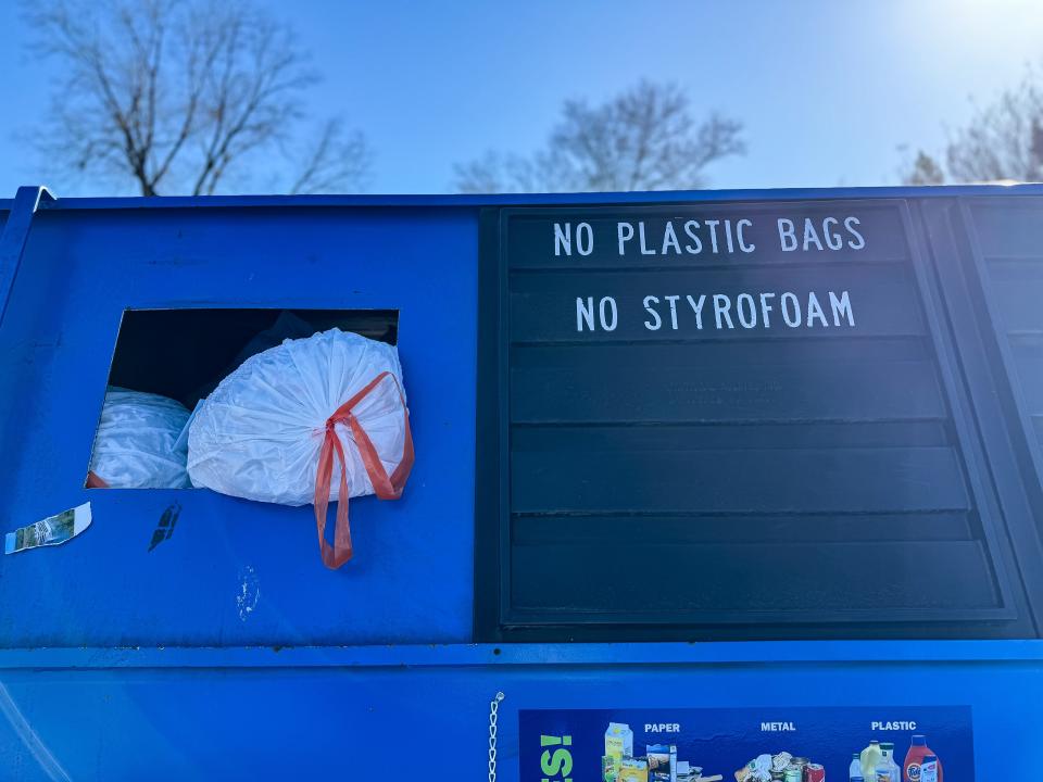 A tied plastic bag sits in a recycling container next to a sign that reads "No plastic bags" in Greenville County.