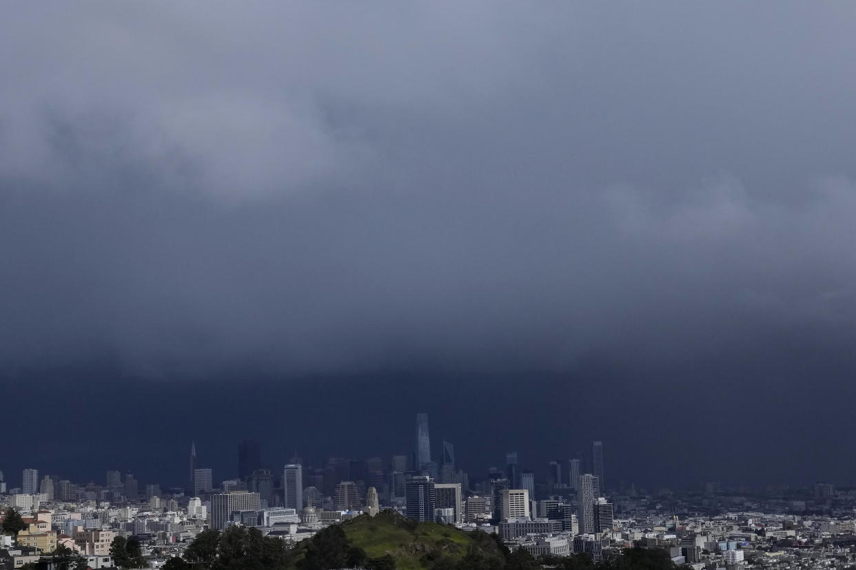 Sun shines on Corona Heights, bottom, as the downtown skyline is obscured by rain clouds in San Francisco, Friday, Feb. 24, 2023. California and other parts of the West are facing heavy snow and rain from the latest winter storm to pound the United States. The National Weather Service has issued blizzard warnings for the Sierra Nevada and Southern California mountains. (AP Photo/Jeff Chiu)