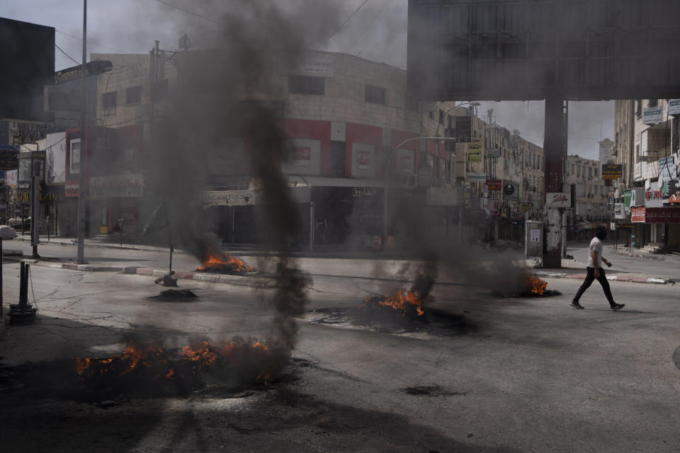 A Palestinian man walks past burning tires during clashes with Israeli forces in the West Bank city of Jenin, Wednesday, May 22, 2024. (AP Photo/Leo Correa)