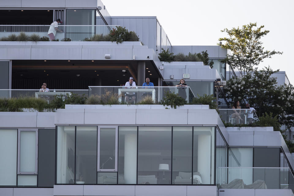 People watch from balconies of a building across the street during an exhibition baseball game between the Washington Nationals and the Philadelphia Phillies at Nationals Park, Saturday, July 18, 2020, in Washington. (AP Photo/Alex Brandon)