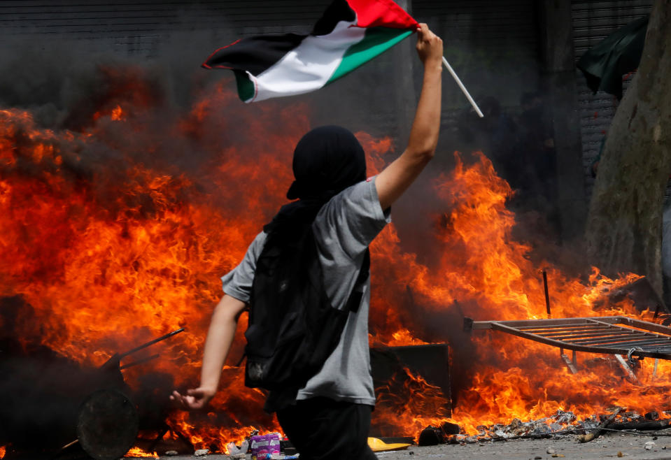 A demonstrator holds a flag as he walks near a fire during a protest against Chile's state economic model in Santiago, Chile on Oct. 23, 2019. (Photo: Henry Romero/Reuters)