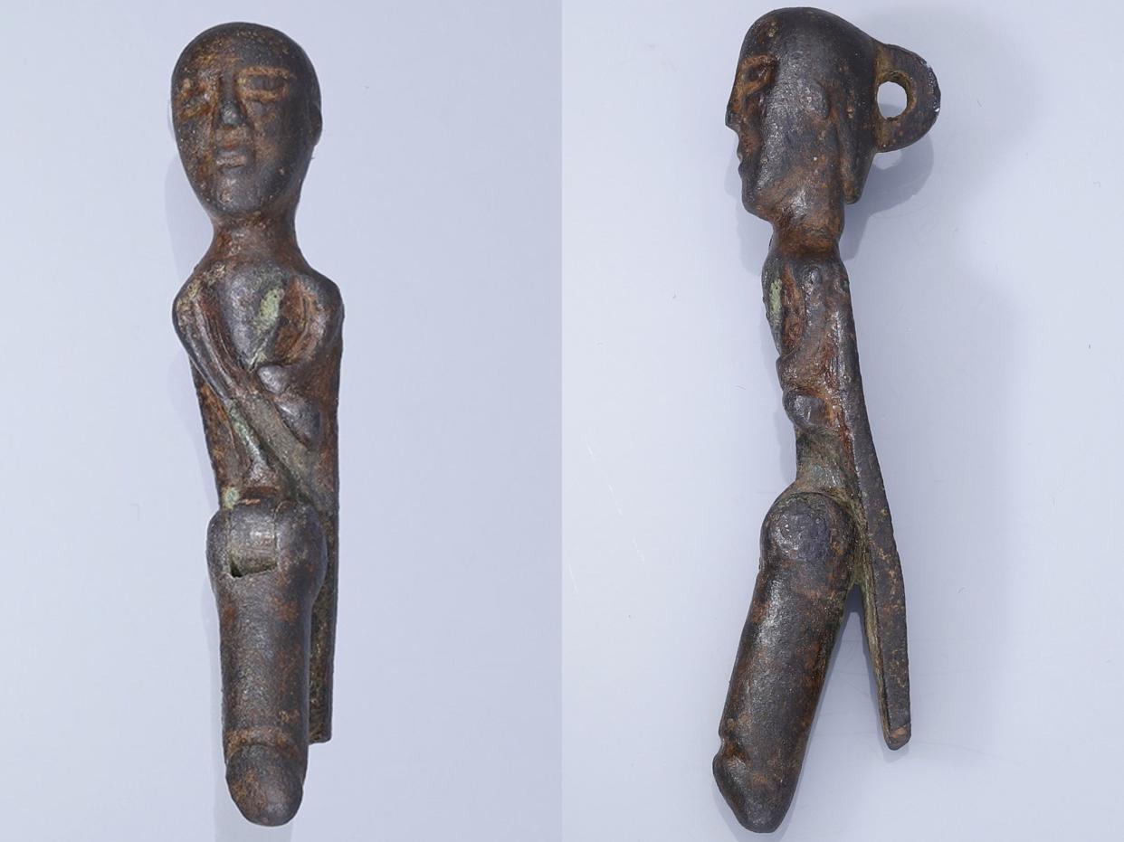 A small bronze statue of a standing man connected to a large bronze phallus in front of him