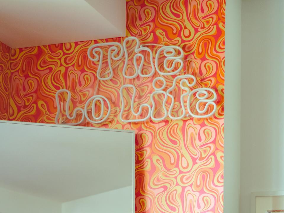 A neon "The Lo Life" sign on a wall with orange-swirl wallpaper