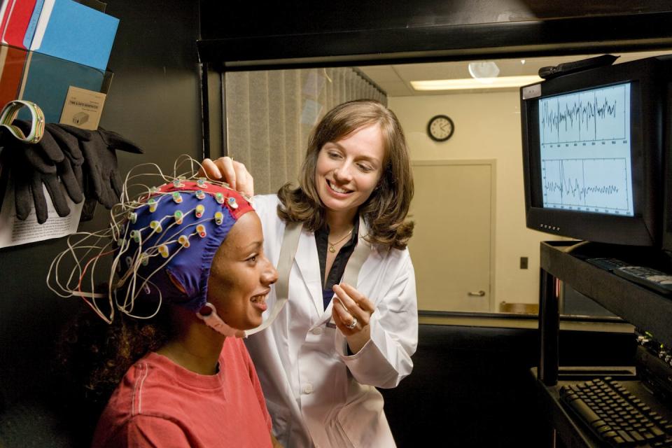 A young woman wearing a hat with electrodes on her head is connected to a computer.