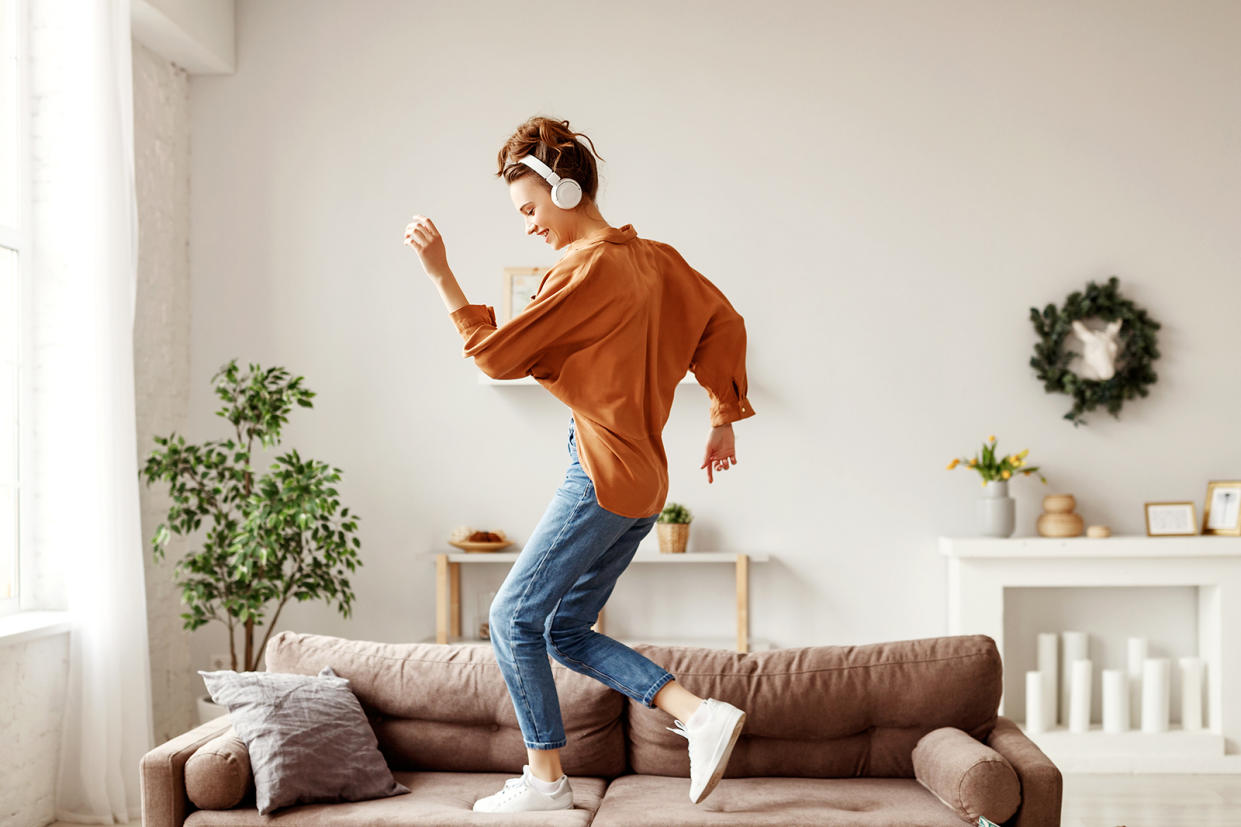 Young woman with headphones standing on couch screaming and dancing