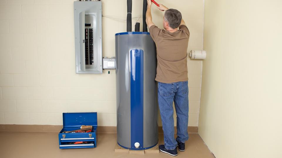 Plumber using a pipe wrench while working on a water heater.