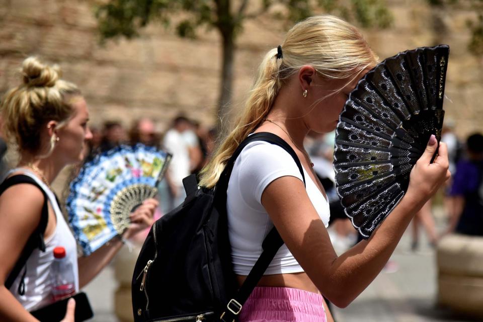 Two women use fans to fight the scorching heat during a heatwave in Seville on June 13, 2022. - Spain was today already in the grips of a heatwave expected to reach "extreme" levels, and France is bracing for one, too, as meteorologists blame the unusually high seasonal temperatures on global warming. (Photo by CRISTINA QUICLER / AFP) (Photo by CRISTINA QUICLER/AFP via Getty Images)