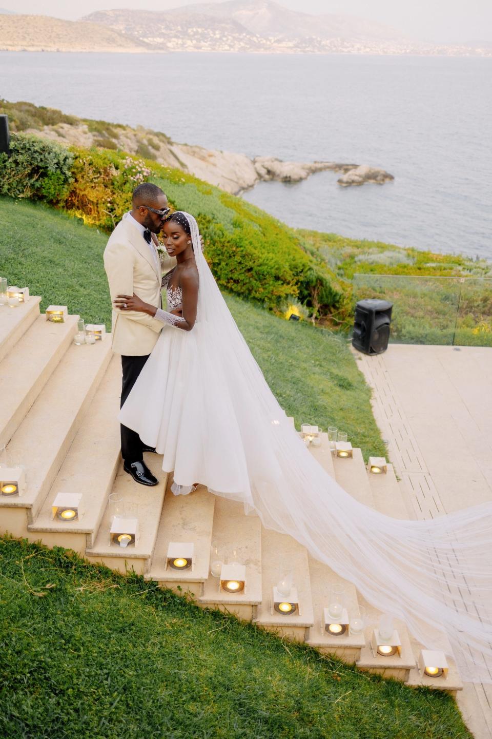 A bride and groom embrace on a staircase with an ocean in the backdrop.