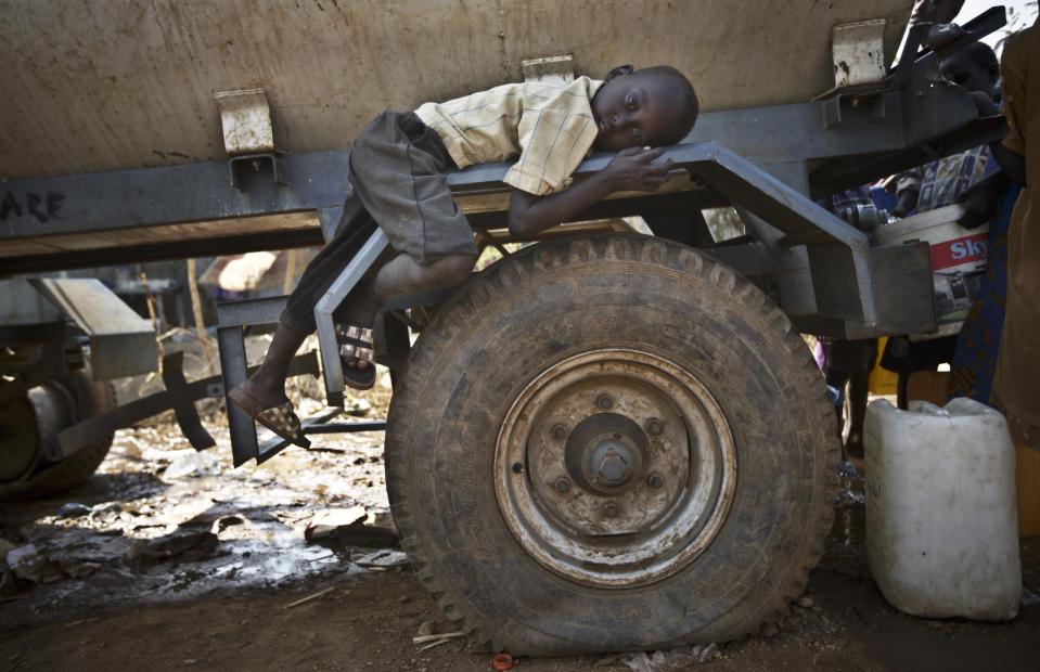 FILE - In this Tuesday, Dec. 31, 2013 file photo, a young displaced boy rests on the wheel arch of a water truck while others fill containers from it, at a United Nations compound which has become home to thousands of people displaced by the recent fighting, in the Jebel area on the outskirts of Juba, South Sudan. The fighting in the world’s newest country has left thousands of its youngest citizens either orphans or separated from their parents, increasing their vulnerability to sickness, malnutrition and recruitment by warring groups as child soldiers. (AP Photo/Ben Curtis, File)