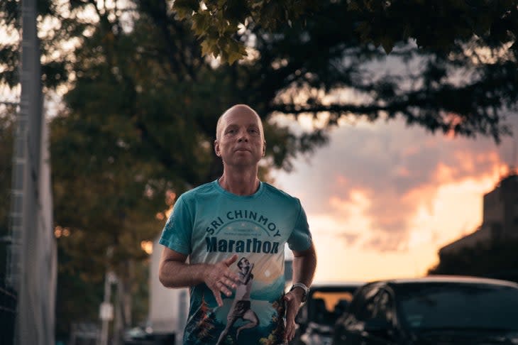 a man runs with a green-blue shirt and sunset behind him