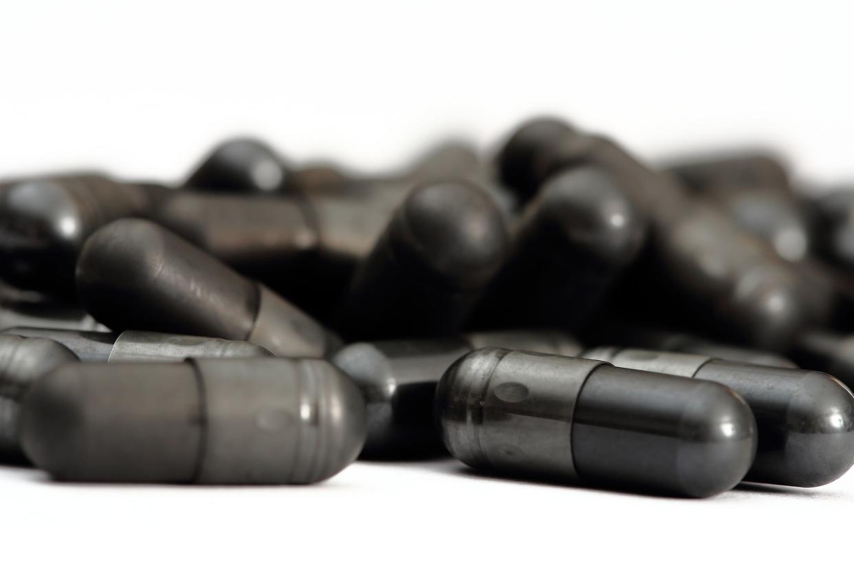 Closeup of activated charcoal capsules in a pile, against white, with a blurred background