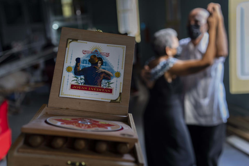 A couple dances next to the Failde Orchestra danzón music album “Joyas Inéditas,” featuring a tobacco box, in Matanzas, Cuba, Saturday, Oct. 2, 2021. “Joyas Inéditas” was launched in two formats: one standard with a typical acrylic case and the other inserted in a wooden box that includes five Cuban cigars. (AP Photo/Ramón Espinosa)