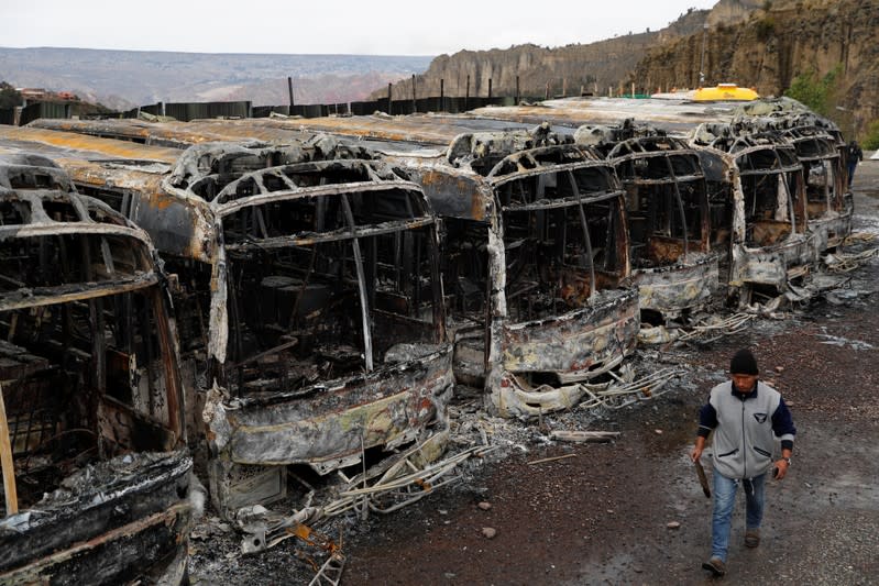 A man walks past buses burned during a protest after Bolivia's President Evo Morales announced on Sunday that he was resigning, in La Paz