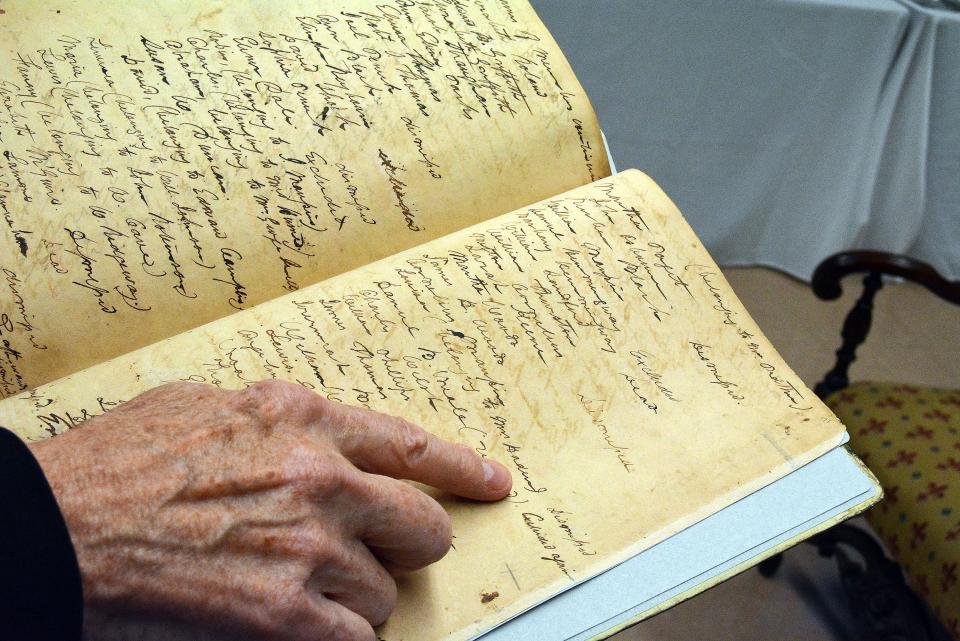 First Baptist Church Historian Ken Hammann holds a restored church journal that includes records of its founding and its darker history. He is pointing to the name of a person enslaved by a church member in the church's early history.