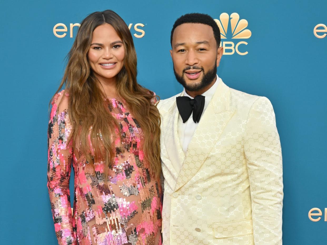 Chrissy Teigen, in a pink sparkly gown, poses with John Legend, in a cream suit and black bow tie, on the red carpet.