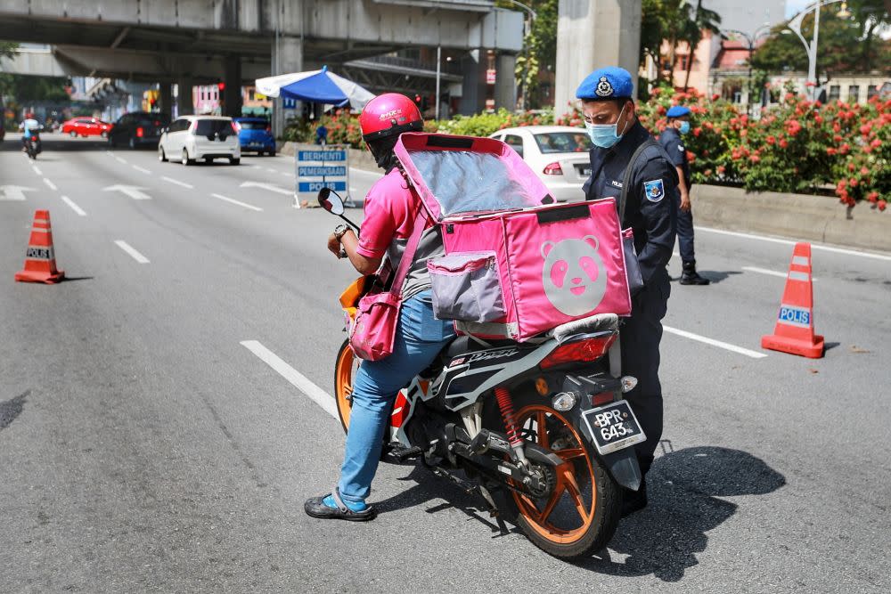 A police personnel conducts checks on a food delivery rider during a road block in Kuala Lumpur April 7, 2020. — Picture by Ahmad Zamzahuri