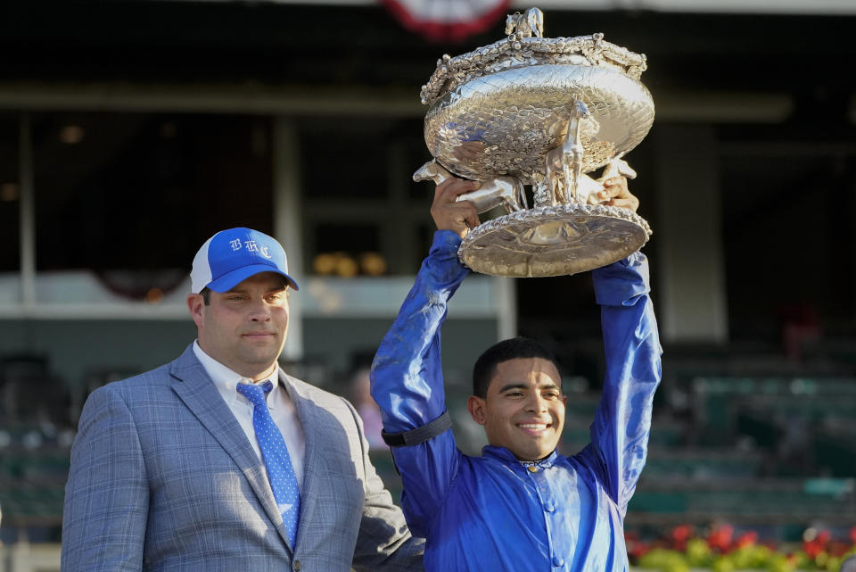 Jockey Luis Saez, right, holds up the August Belmont Trophy with Brad Cox after winning the 153rd running of the Belmont Stakes horse race with Essential Quality (2), Saturday, June 5, 2021, at Belmont Park in Elmont, N.Y. (AP Photo/John Minchillo)