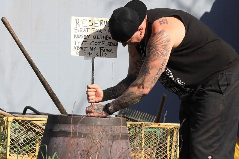 Jason Windus colocando un cartel en el jardín de su casa avisándole al vecino que esta es su venganza. (Kent Porter/The Press Democrat via AP)