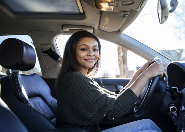 A woman smiling as she sits in the driver's seat of a car with her seatbelt on