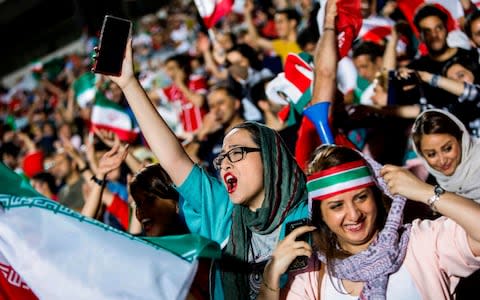 Iranian football supporters wave their national flags as they cheer for their team - Credit: STRINGER/AFP/Getty Images