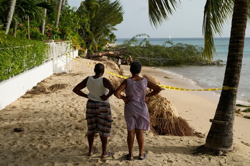 Two neighbors look out at beach erosion and a fallen tree the day after Hurricane Beryl