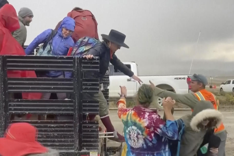 En una imagen tomada de un video proporcionado por Rebecca Barger, varias personas reciben ayuda el lunes 4 de septiembre de 2023 para descender de la parte trasera de una camioneta en la sede del festival contracultural Burning Man, en Black Rock, Nevada. (Rebecca Barger/@rebeccabargerphoto vía AP)