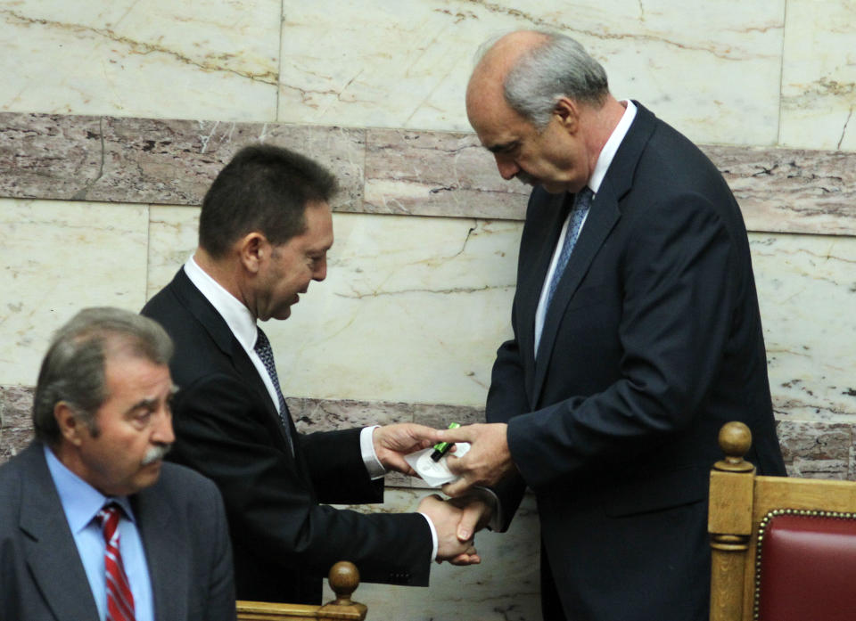 Greece's Finance Minister Yannis Stournaras, left, gives a disc containing the new draft state budget for 2013 to Parliament speaker Evangelos Meimarakis, right, at the Greek parliament in Athens, Wednesday, Oct. 31, 2012. Greek lawmakers are to vote Wednesday on a privatization bill that will be the first major test for the country's troubled governing coalition, while journalists have walked off the job at the start of rolling 24-hour strikes to protest austerity plans that will affect their healthcare funds. (AP Photo/Thanassis Stavrakis)