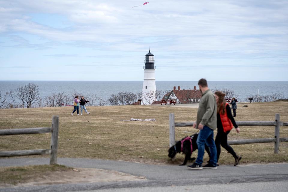 A couple with a dog are seen with a lighthouse in the background.