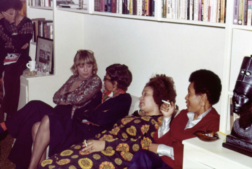 Angela Davis and three others sit and converse in a relaxed setting with bookshelves in the background