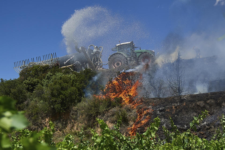 A neighbour with a tractor sprays water on a fire in San Martin de Unx in northern Spain, Sunday, June 19, 2022. Firefighters in Spain are struggling to contain wildfires in several parts of the country which as been suffering an unusual heat wave for this time of the year. (AP Photo/Miguel Oses)