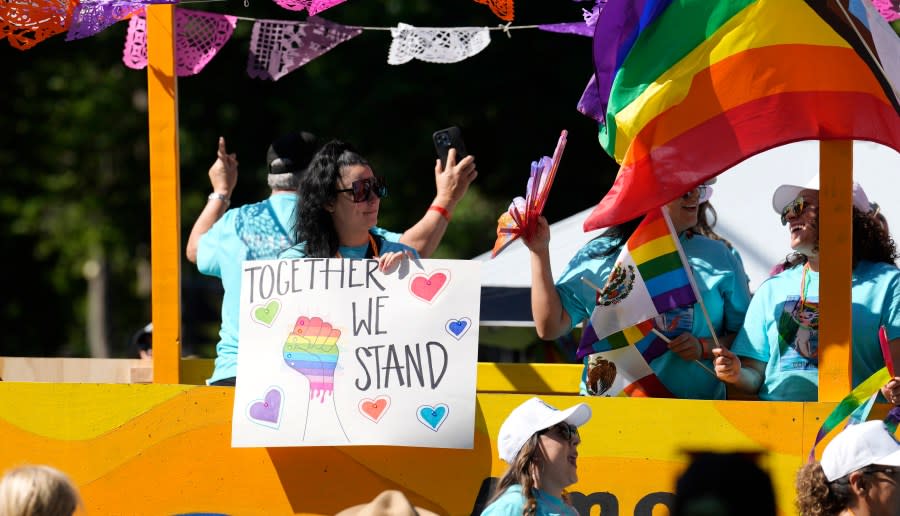 Participant holds a placard while riding a float in the Pride parade through the streets of downtown Sunday, June 25, 2023, in Denver. (AP Photo/David Zalubowski)