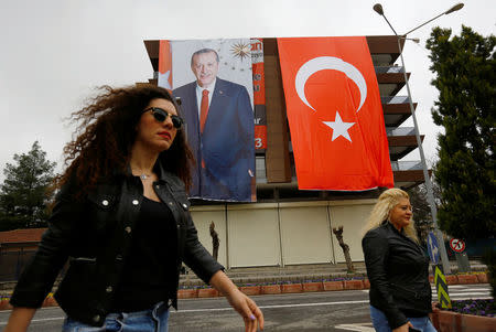 People walk past by a building which is decorated by a poster of Turkish President Tayyip Erdogan and a Turkish flag before a rally for the upcoming referendum in the Kurdish-dominated southeastern city of Diyarbakir, Turkey, April 1, 2017. REUTERS/Murad Sezer