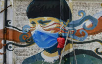 A street artist spray paints a protective face mask over an old mural featuring a Venezuelan Indigenous man, in Caracas, Venezuela, Saturday, July 18, 2020, amid the new coronavirus pandemic. (AP Photo/Matias Delacroix)