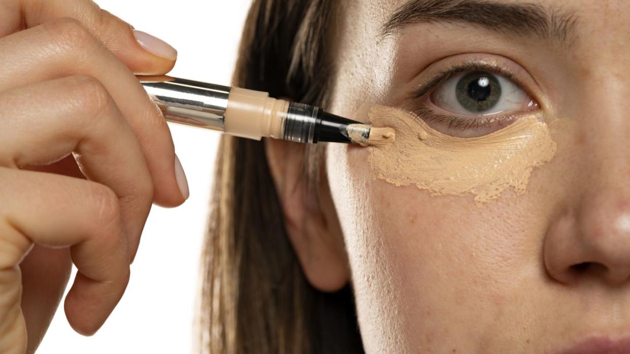 close up of a young women applying concealer under her eyes