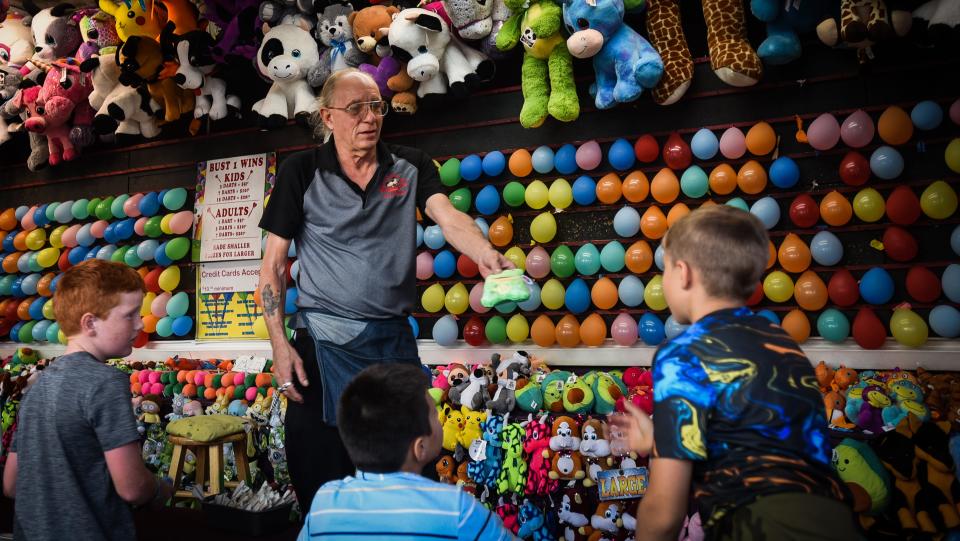 Carnival worker Stephen "Spider" Stimpson hands a youngster  a prize Tuesday, July 13, 2022, on the fairway at the Eaton County Fair in Charlotte. Stimpson has worked carvivals and fairs for 47 years.