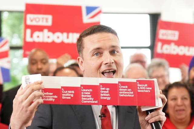 Wes Streeting smiles as he holds up a Labour pledges card with supporters and 'Vote Labour' banners in the background