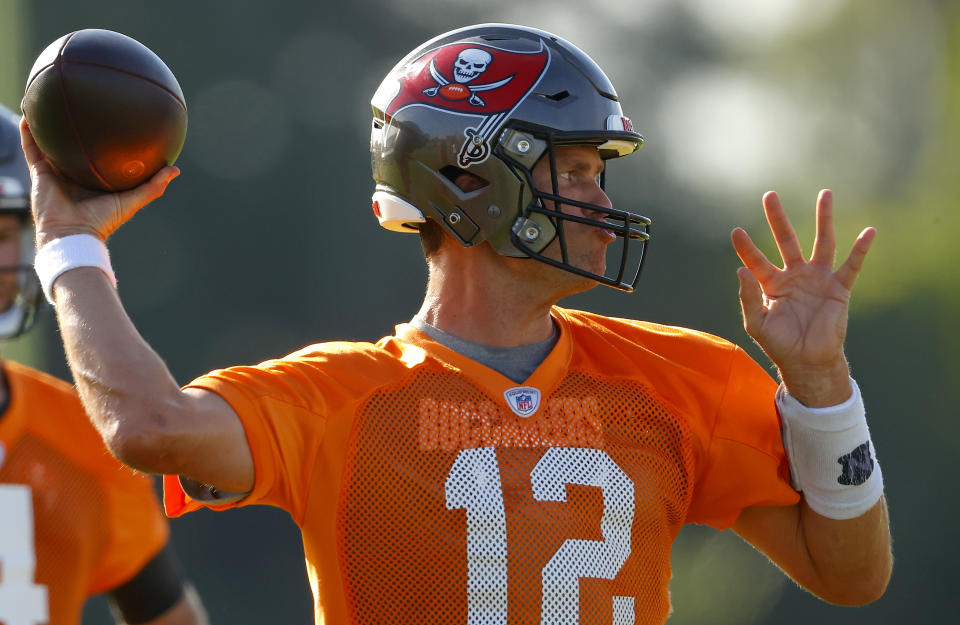 Tom Brady throws a football during training camp wearing a gray helmet with the Buccaneers logo on it.