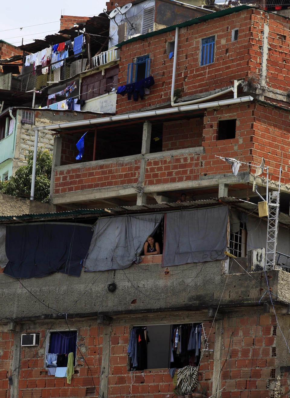 In this Sept. 16, 2012 photo, a woman looks out from her cinderblock home as opposition presidential candidate Henrique Cariles campaigns in the Petare shantytown of Caracas, Venezuela. From single mothers to construction workers, a segment of President Hugo Chavez supporters have been turning away from the president and instead considering new leadership. They've become key to the Oct. 7 presidential vote and Capriles' strategy. (AP Photo/Fernando Llano)