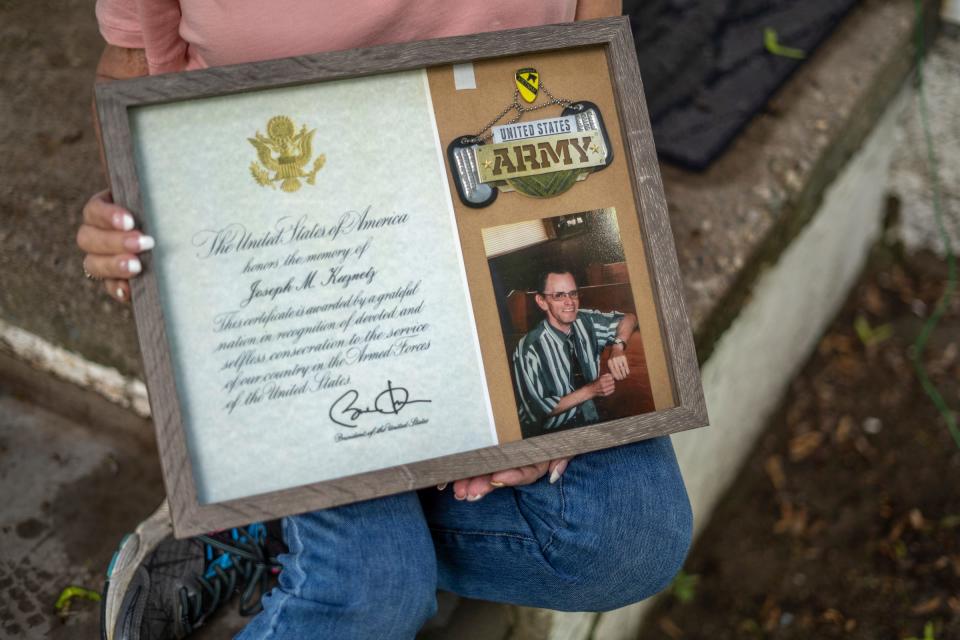 Theresa Kuznetz, of Wyandotte, sits at her home in Wyandotte on May 27, 2022, with a photo of her late husband, Army veteran Joseph Kuznetz, who passed away on Jan. 31, 2011, from lung cancer due to Agent Orange. Kuznetz will be traveling to Washington D.C. to announce her late husband's name as 25 Michigan Vietnam veterans are being honored in D.C. by the Vietnam Veterans Memorial Fund.