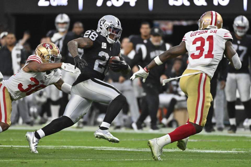 Las Vegas Raiders running back Josh Jacobs (28) tries to evade tackles by San Francisco 49ers cornerback Deommodore Lenoir (38) and safety Tashaun Gipson Sr. (31) during the first half of an NFL football game between the San Francisco 49ers and Las Vegas Raiders, Sunday, Jan. 1, 2023, in Las Vegas. (AP Photo/David Becker)