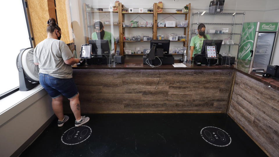 In this Wednesday, June 24, 2020, photograph, Kerri Thibodeau, of Stoughton, Mass., makes a purchase at Pure Oasis, a Black-owned recreational marijuana dispensary, in the Grove Hall neighborhood of Boston. Many from outside Boston have recently shopped and supported the store which was robbed and vandalized earlier in the month. (AP Photo/Charles Krupa)