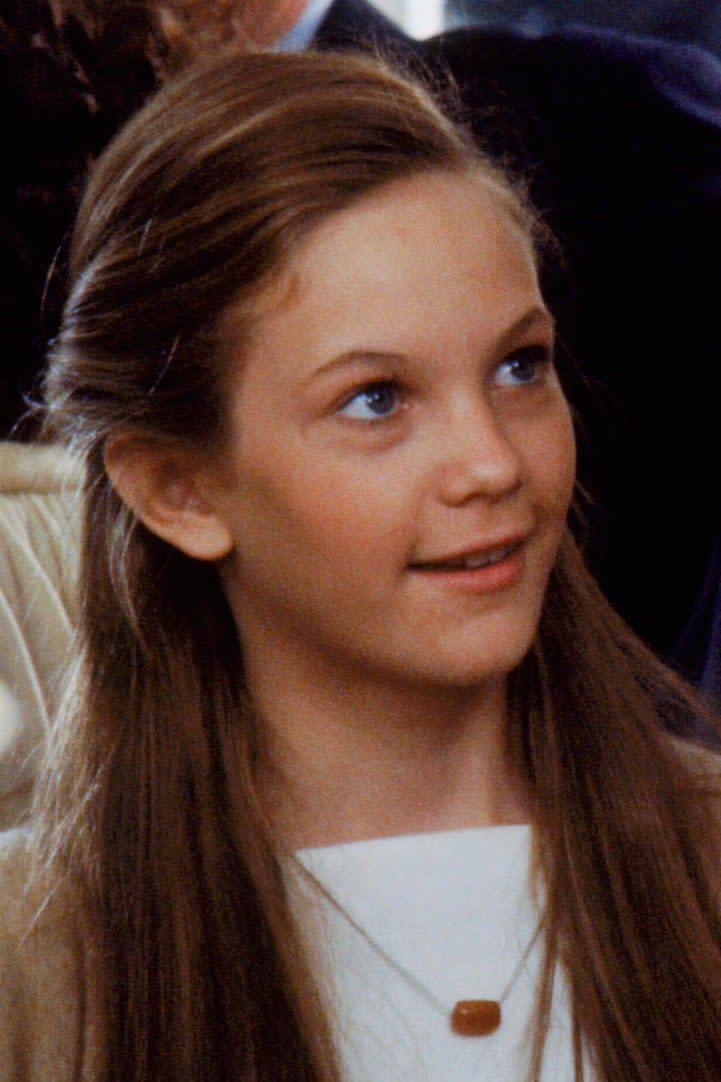 A group of people smiling and conversing at a social event. An older gentleman in a gray suit and a young Diane Lane with a striped shirt are in focus