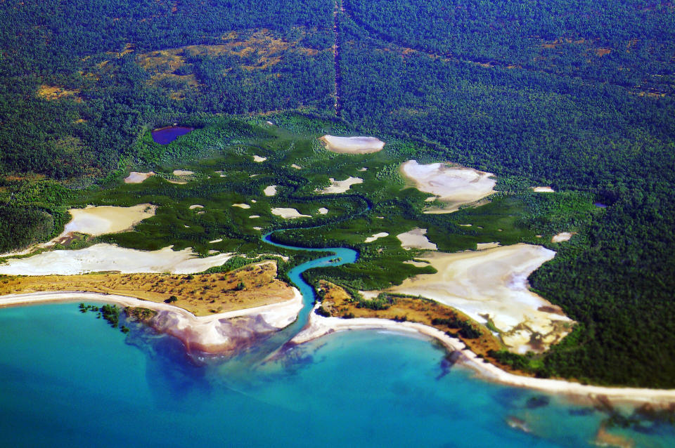 aerial photo of salt flats on the outskirts of Darwin, Northern Territory, Australia. A small tidal stream drains a mangrove forest with sand dunes and salt flats forming this tidal ecosystem.