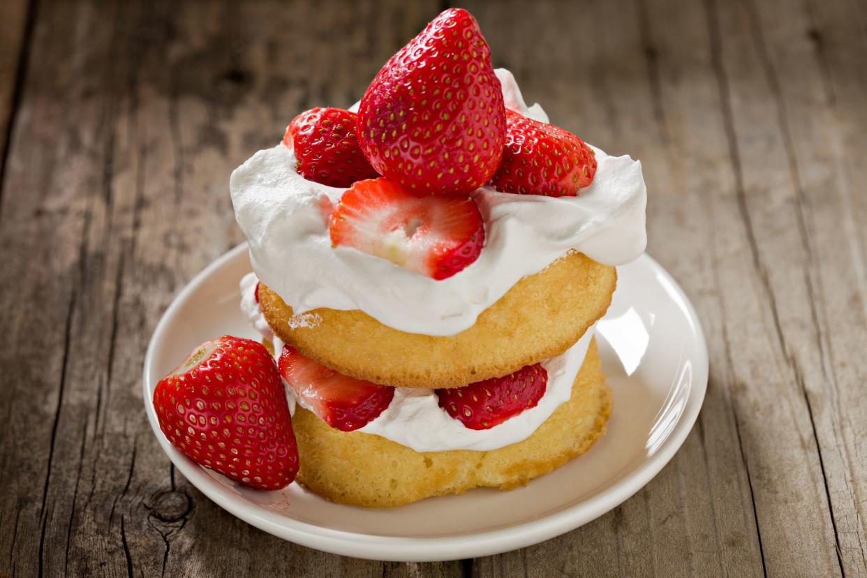 An extreme close up of a small white bowl with a strawberry shortcake. Shot on an grungy old wooden picnic table