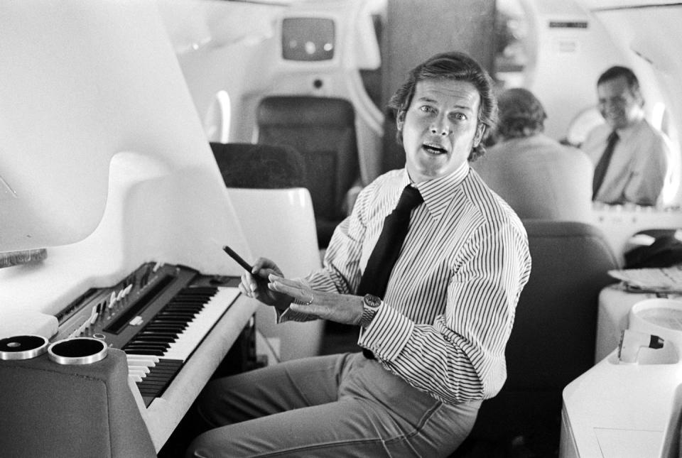 <p>Roger Moore plays an electric keyboard onboard a private jet in 1975. </p>