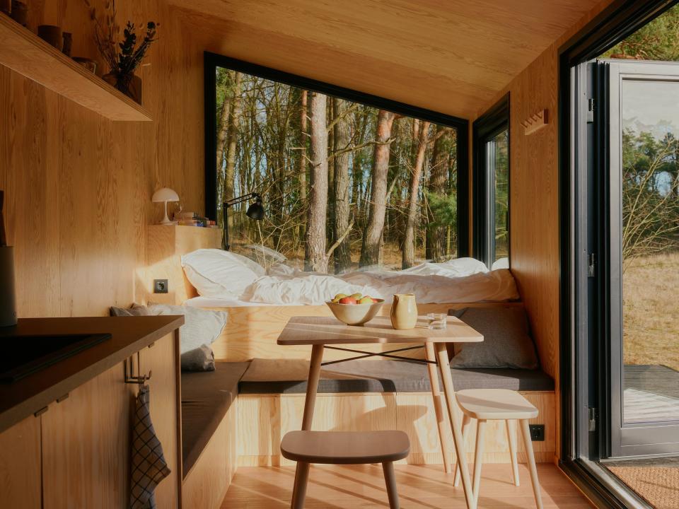 A bed, kitchen, table with chairs and windows showing nature outside