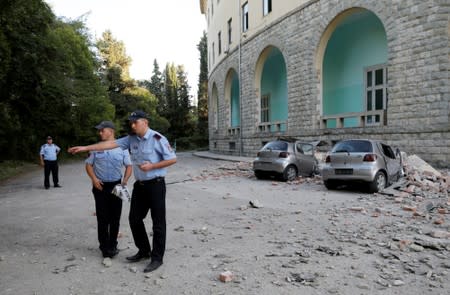 Police officers secure the area next to destroyed cars and a damaged building after an earthquake in Tirana