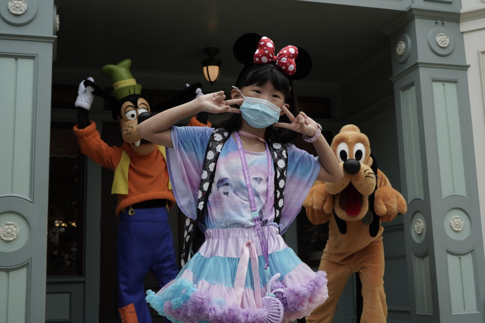 A visitor wearing a face mask take a selfie with the iconic cartoon characters Goofy and Pluto at the Hong Kong Disneyland, Friday, Sept. 25, 2020. Hong Kong Disneyland reopened its doors to visitors after closed temporarily due to the coronavirus outbreak. (AP Photo/Kin Cheung)