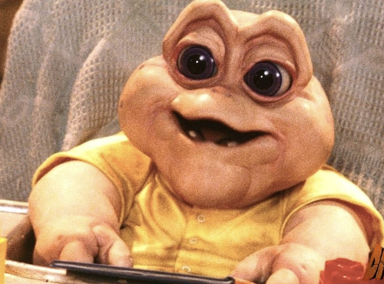 Baby Sinclair puppet from the TV show "Dinosaurs" sitting with a spoon in hand